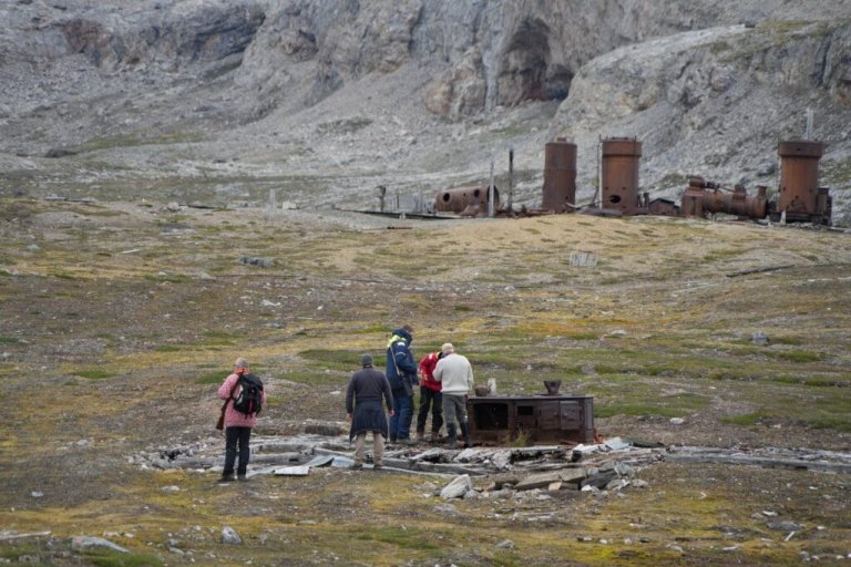 Visitors stand in the remains of a cabin at the site of the abandoned marble mine on Blomstrandhalvøya in Kongsfjorden, unaware of the damage they may be doing to the old wooden floor. Photo: Anne-Cathrine Flyen / Norwegian Institute for Cultural Heritage Research