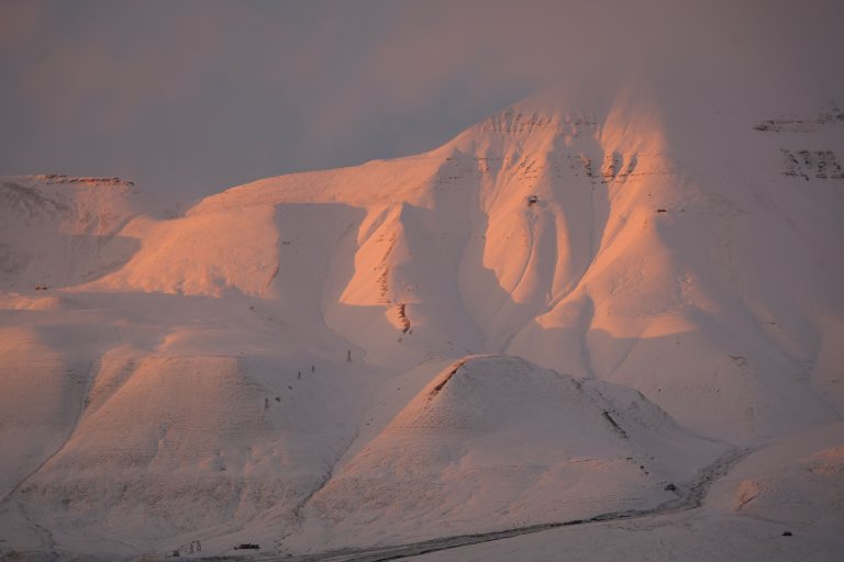 Cableway pylons at Hiorthhamn in snow and sunset. The wooden structure around the mine opening and the miners’ living quarters can be seen high up on the mountainside on the two sunlit ridges to the right. Photo: Anne-Cathrine Flyen / Norwegian Institute for Cultural Heritage Research