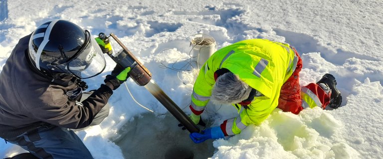 Erling Fjelldal fra NIBIO Svanhovd (med scooterhjelm) og Geir Dahl-Hansen fra Akvaplan-niva tar sedimentprøver i Firkantvann. Foto: Tore Flatlandsmo Berglen, NILU