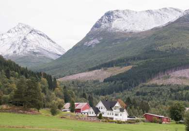 Gård med snødekte fjell og skog i bakgrunn